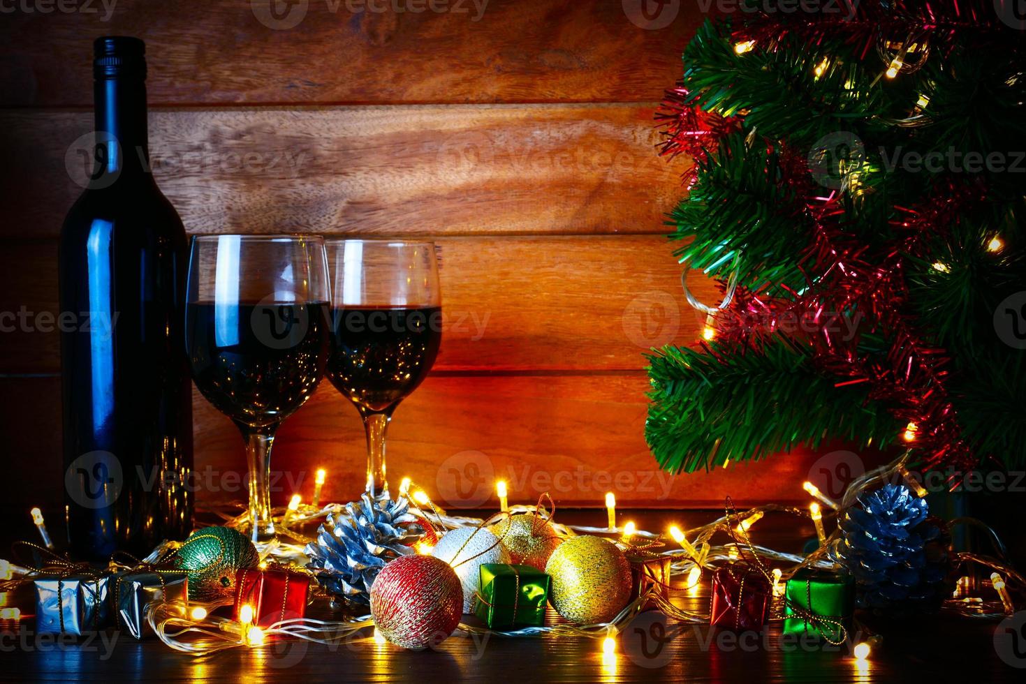 vino tinto en vidrio transparente, árbol de navidad y adorno en mesa de madera listo para celebrar. foto