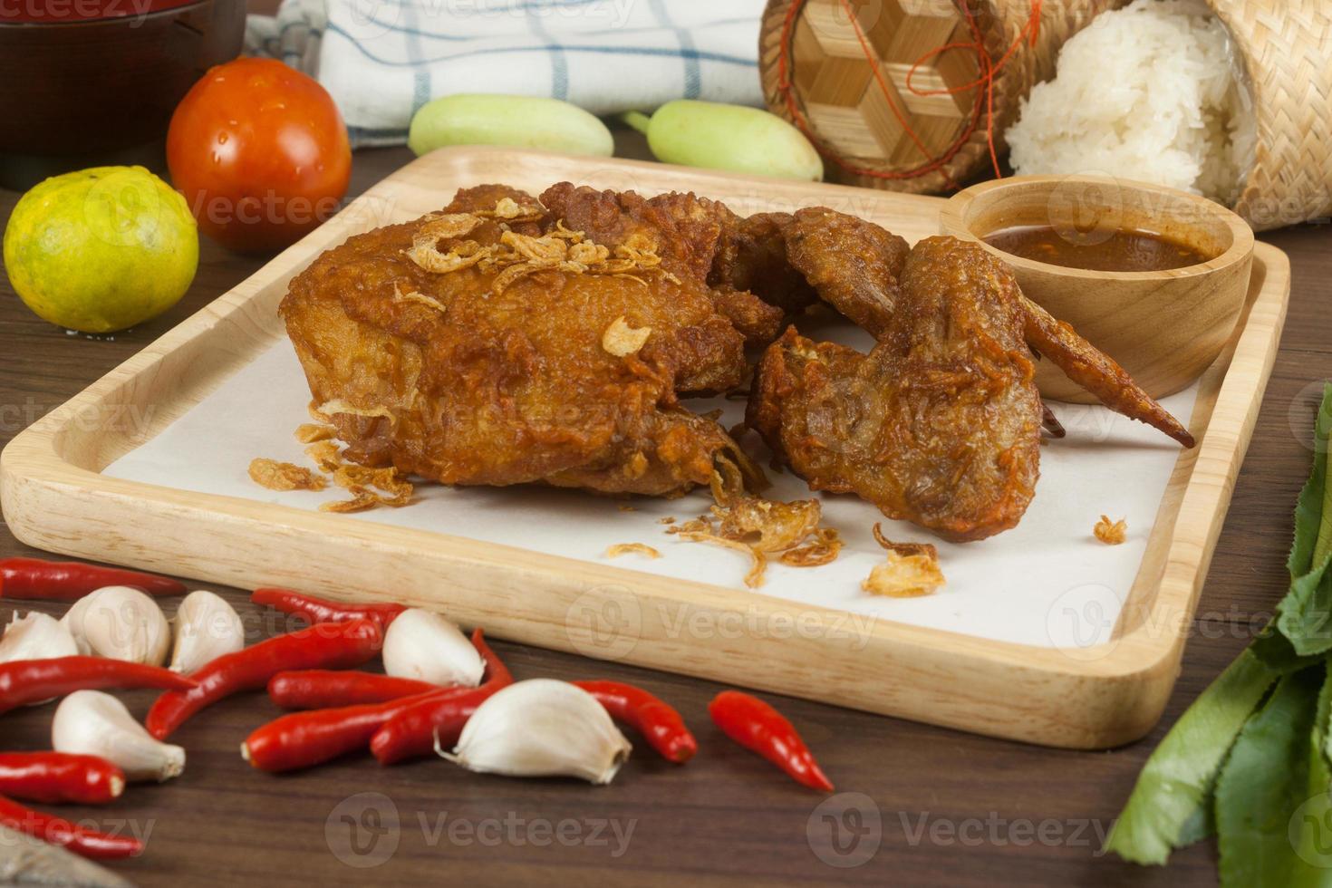 Fried chicken with spices on wooden plate with sauce and vegetables photo