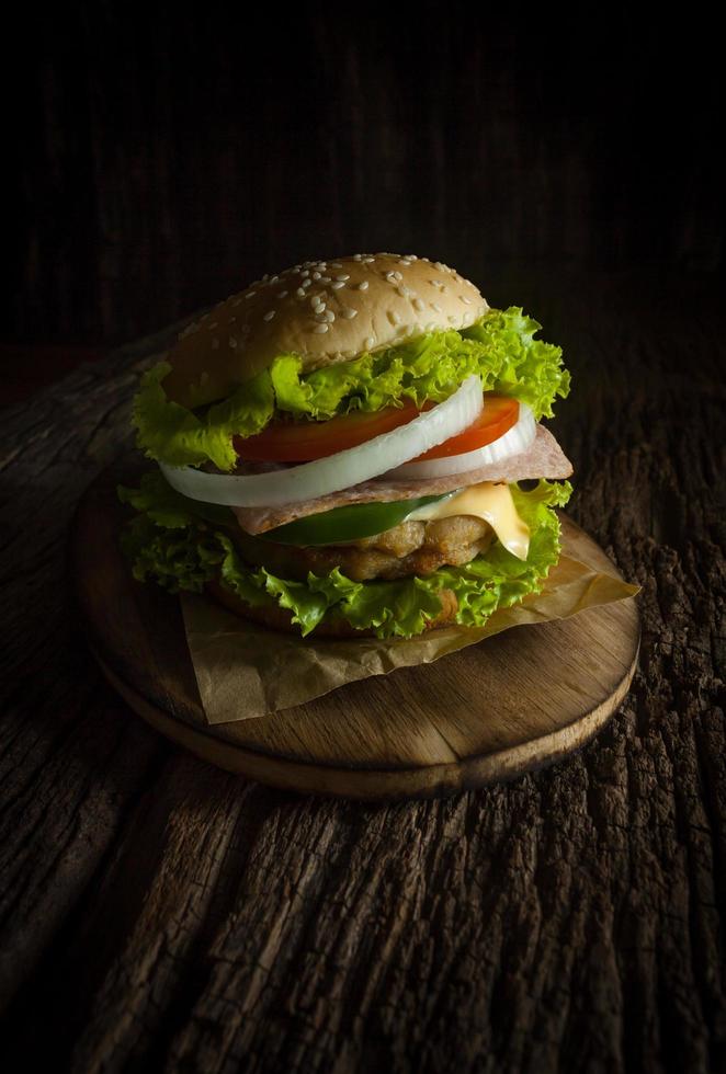 Pork hamburger Homemade with grilled bacon contains vegetables, cheese, lettuce, onion, chilli, spices in a wooden dish on a wooden floor. photo