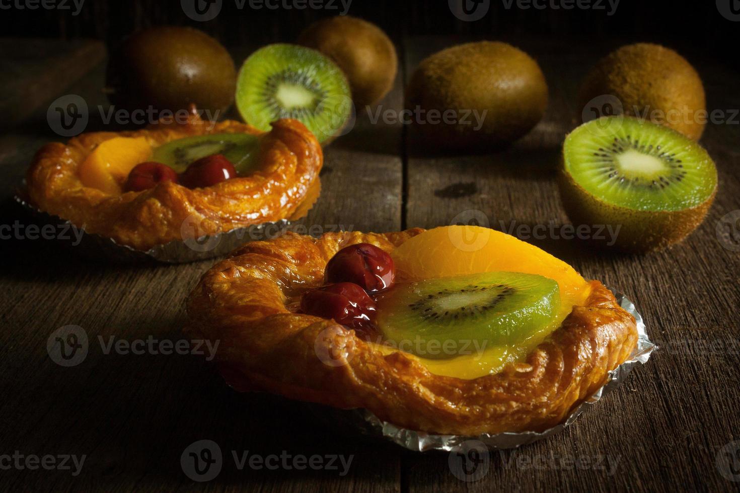 tarta de frutas con kiwi, cereza, caqui, puesta sobre una tira de acero en el banco de madera con fondo negro foto