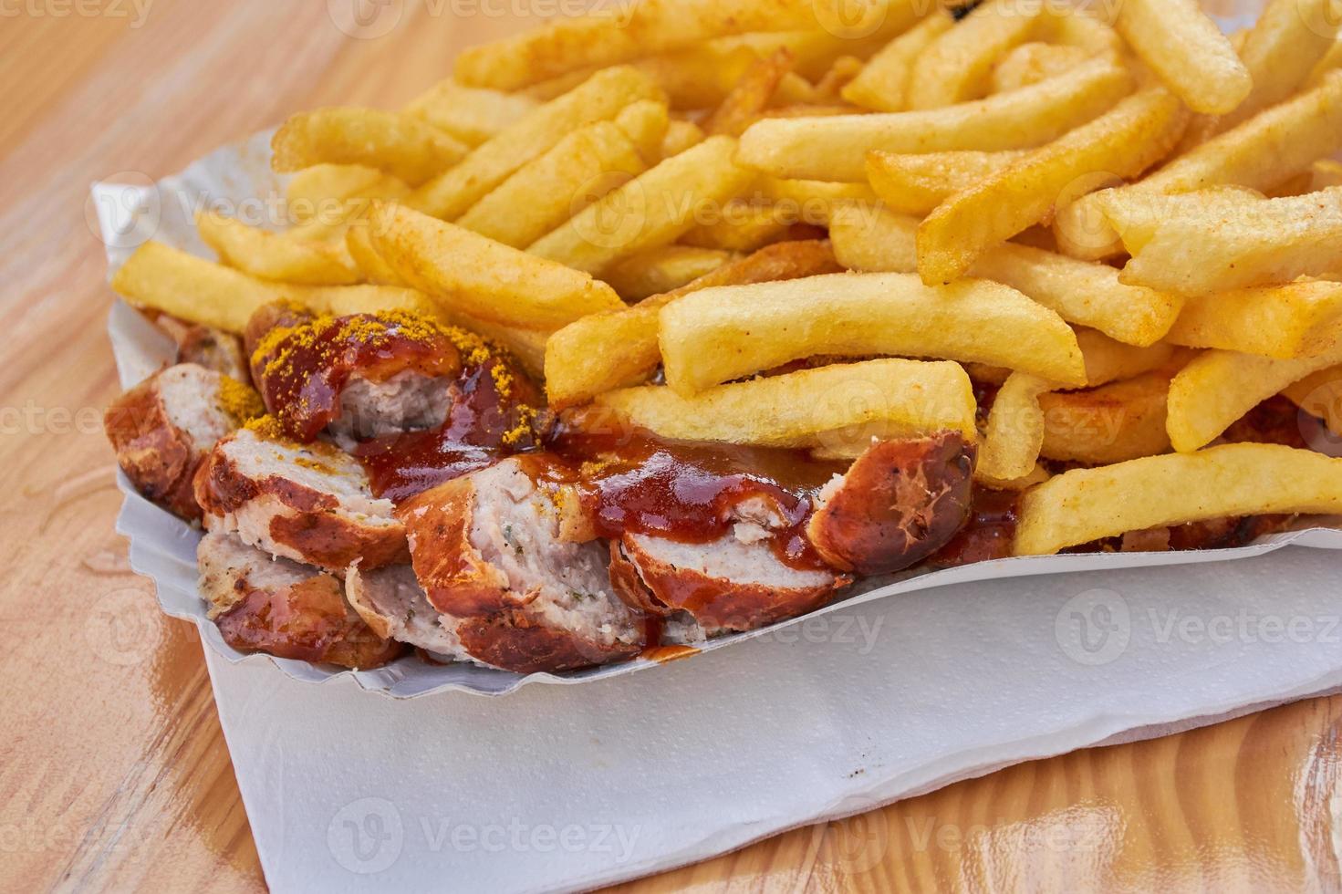 salchicha currywurst alemana con ketchup de curry y papas fritas en una mesa marrón en un parque