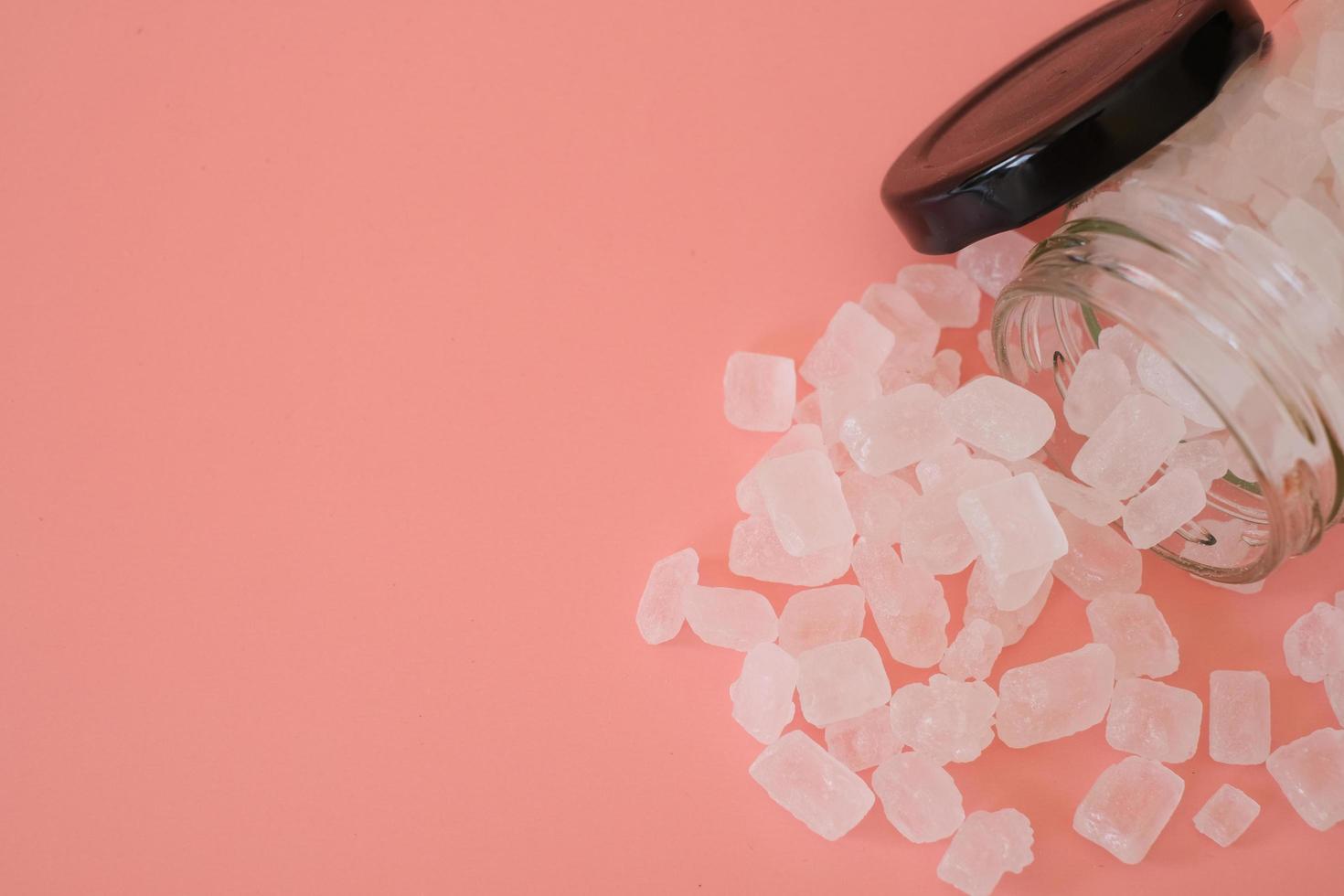 White candy rock sugar or crystal sugar in glass jar isolated on pink background. White rock sugar is melted and then allowed to crystallize into semi-translucent gemstone. photo