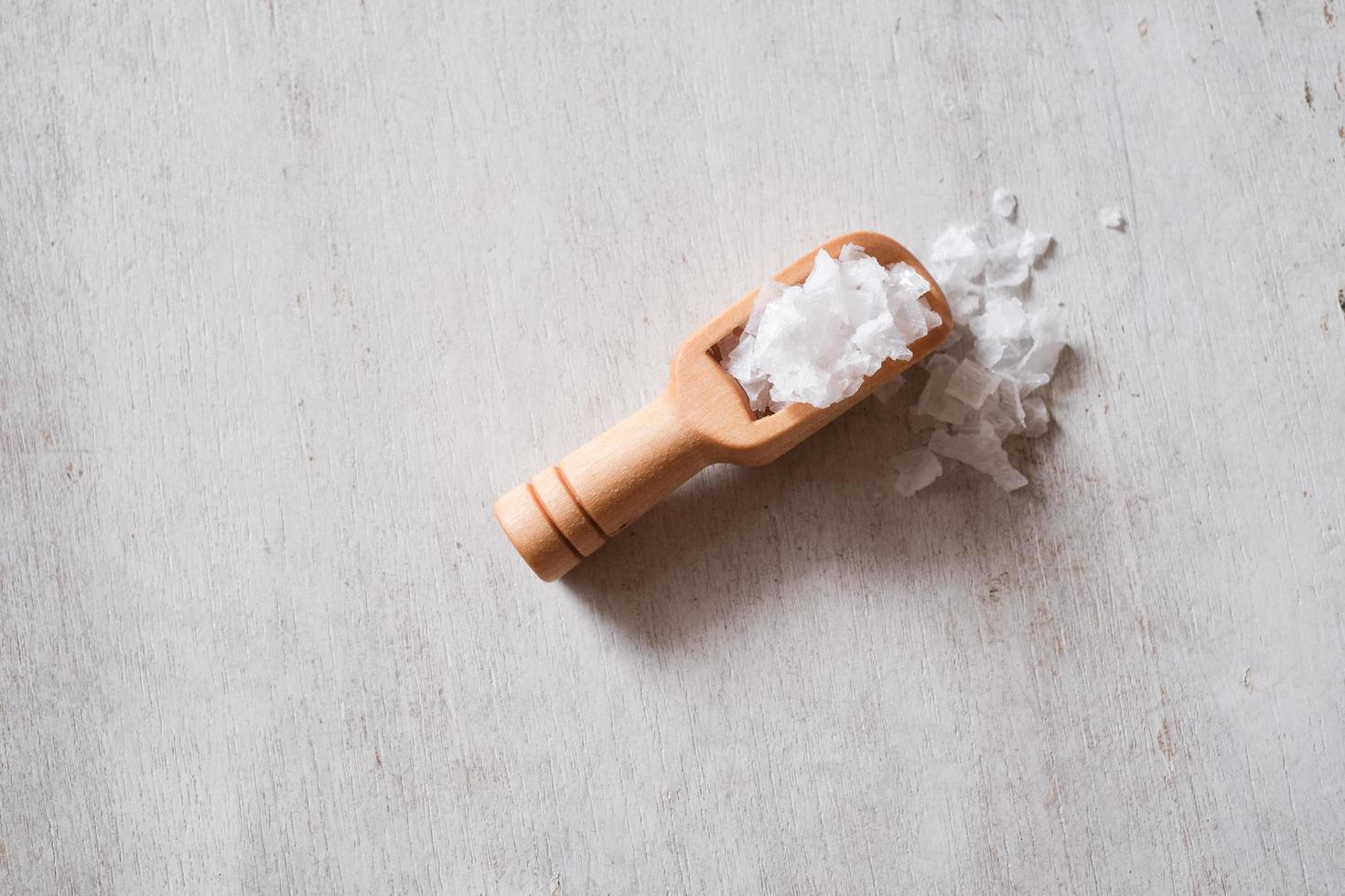 Flower of salt, is a salt that forms as a thin, delicate crust on the surface of seawater in the wooden scoop on wooden background. photo