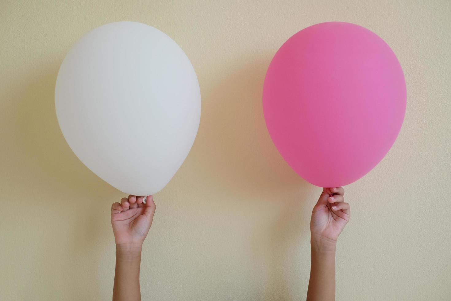 cierre el niño de la mano sosteniendo el globo blanco y rosa aislado en el fondo blanco. foto