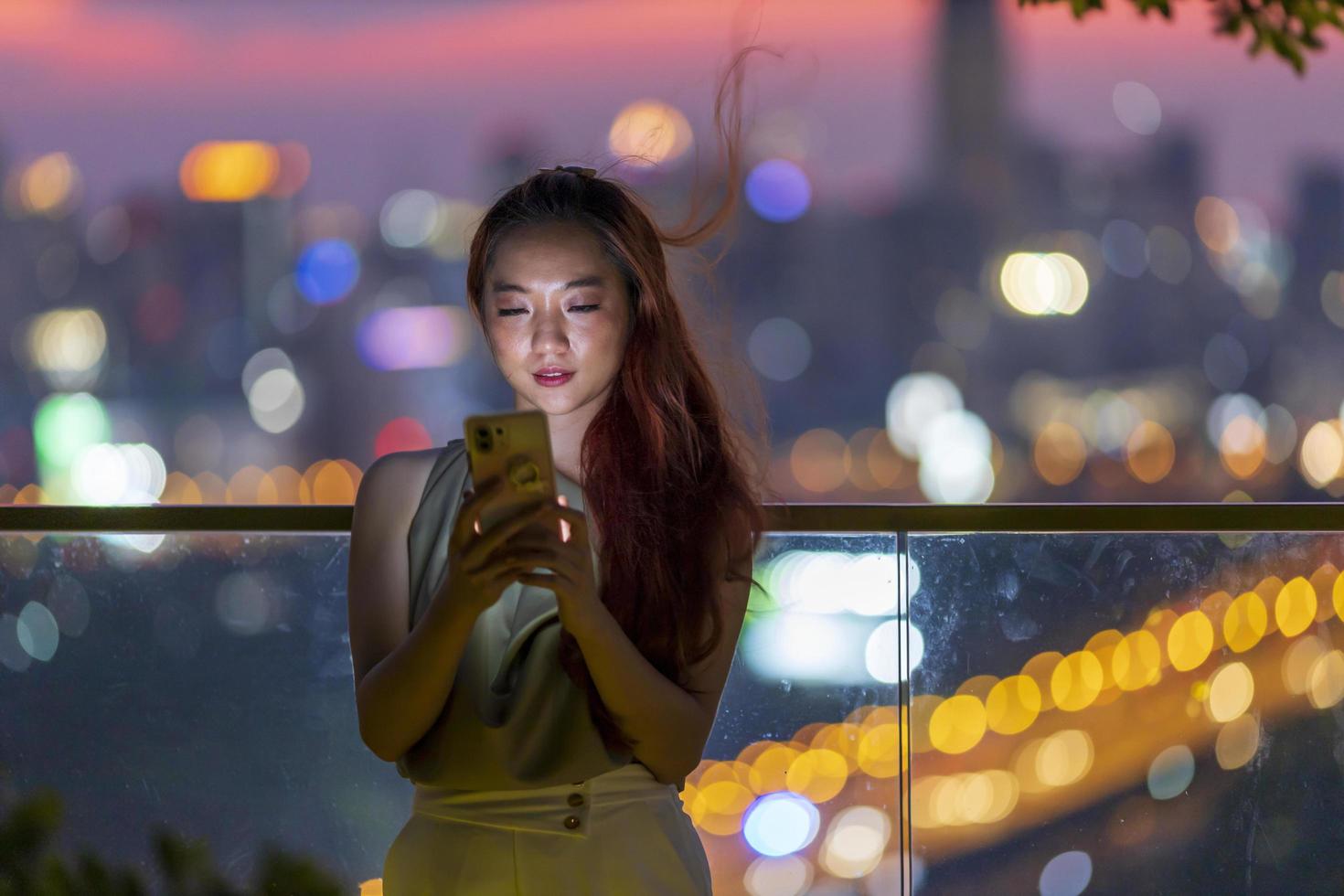 Asian woman using mobile phone with Bangkok skyscraper cityscape at sunset blue hour at downtown urban district for modern luxury living and prestige travel concept photo