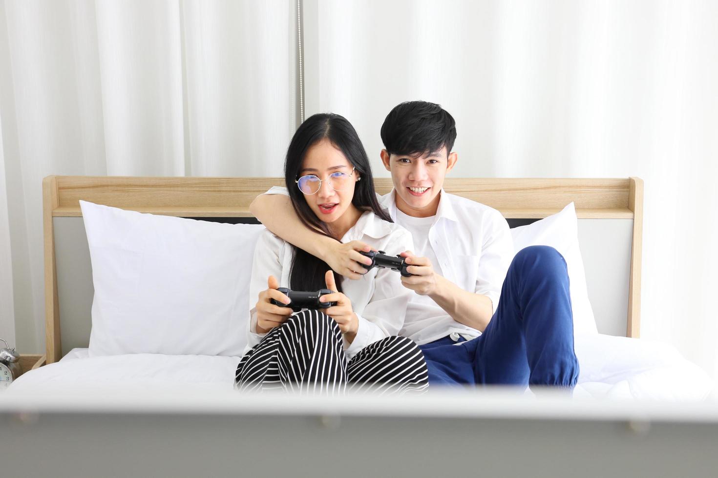 Asian couple having fun playing video game console together in bed with copy space for E-Sports and online gamer concept photo