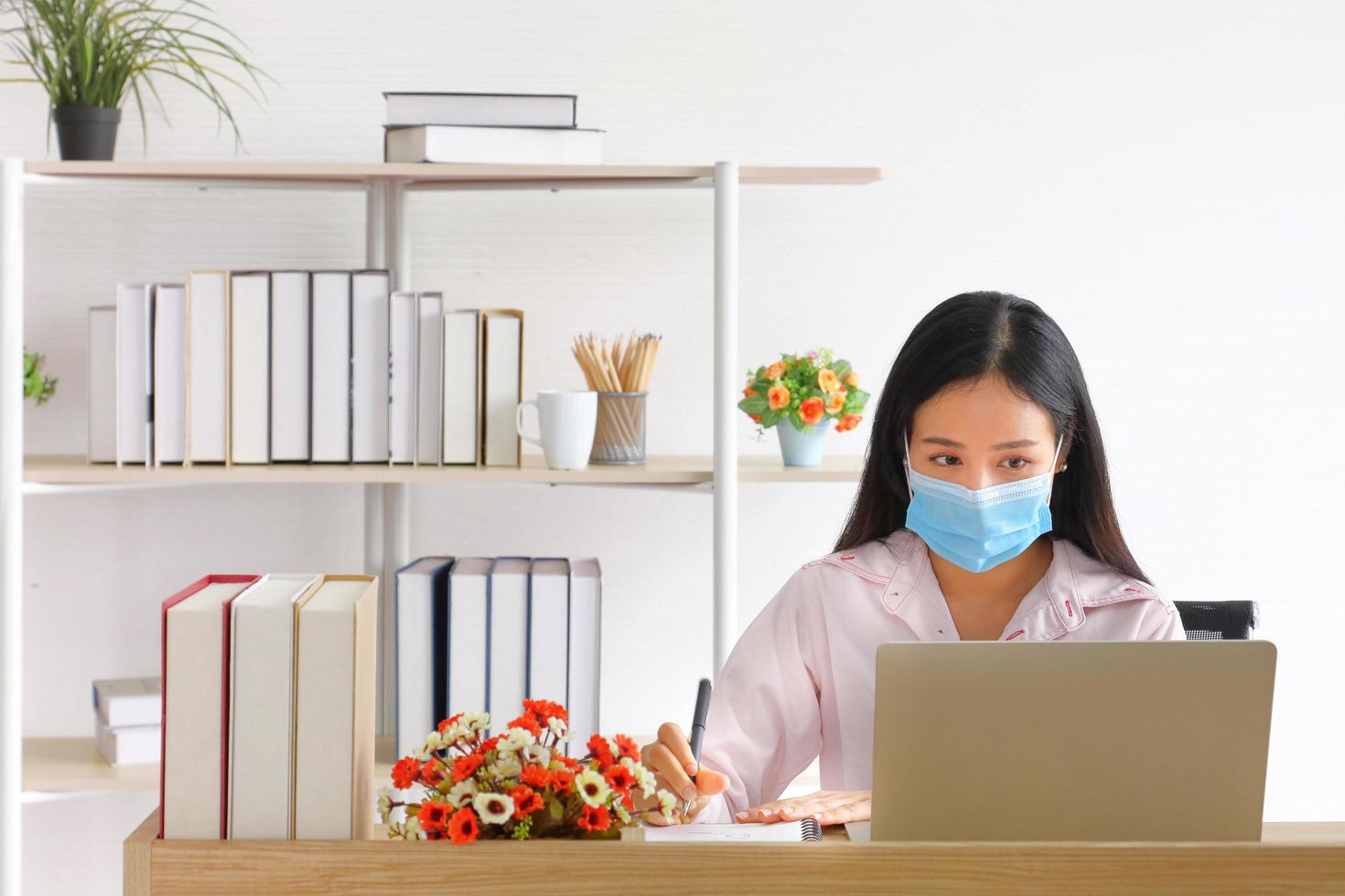 Female employee wearing medical facial mask working from home as social distancing policy in the business office during new normal change after coronavirus or post covid-19 with copy space photo