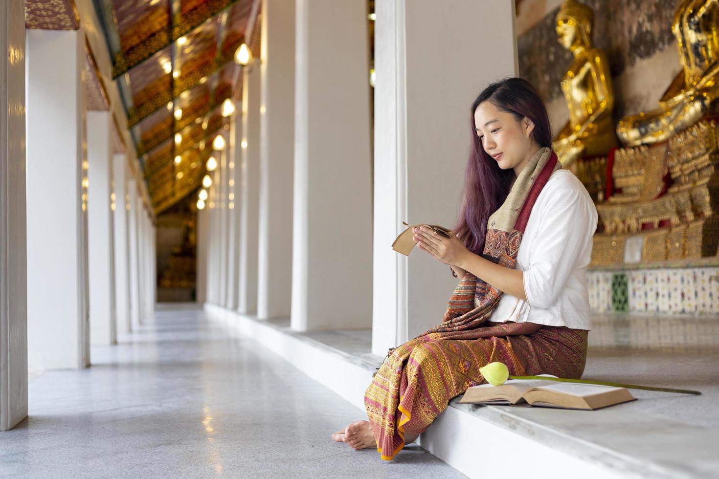 Asian buddhist woman is reading Sanskrit ancient palm leaf manuscript of Tripitaka the Lord Buddha dhamma teaching while sitting in temple on holy full moon day to chant and worship in the monastery photo