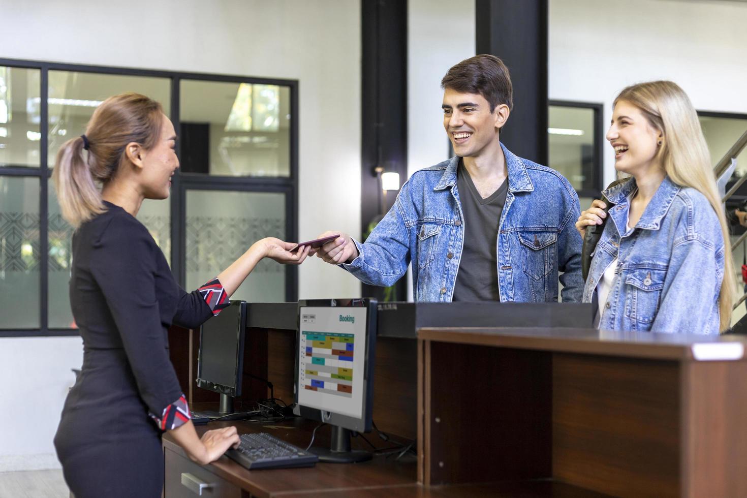 Caucasian tourist couple is handing passport to the reception at hotel lobby counter for check in to the room for international travel and vacation concept photo