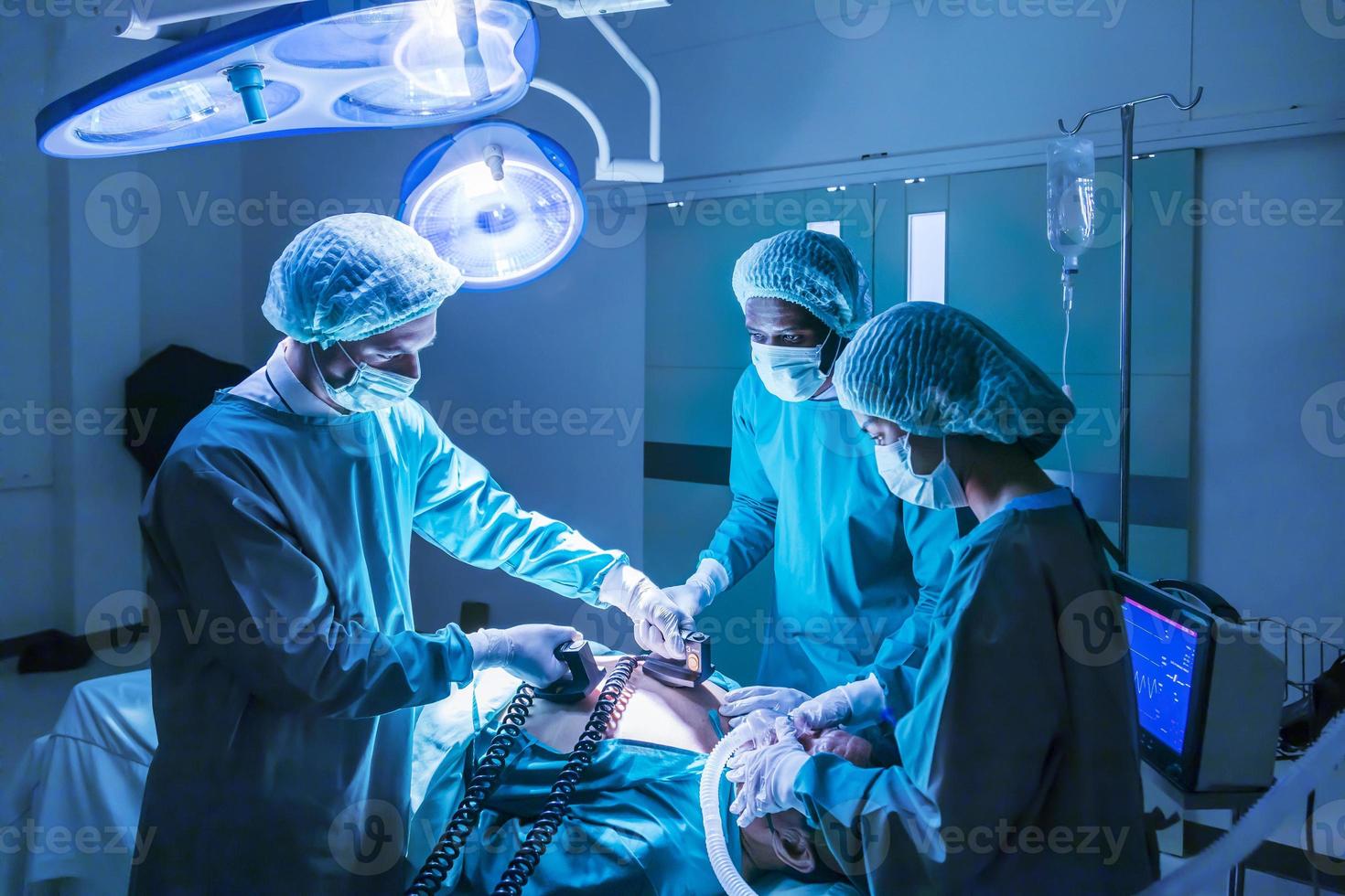 Team of surgeon doctor using defibrillator to give electrical shock to patient heart who is suffering from cardiac arrest in emergency surgical room photo