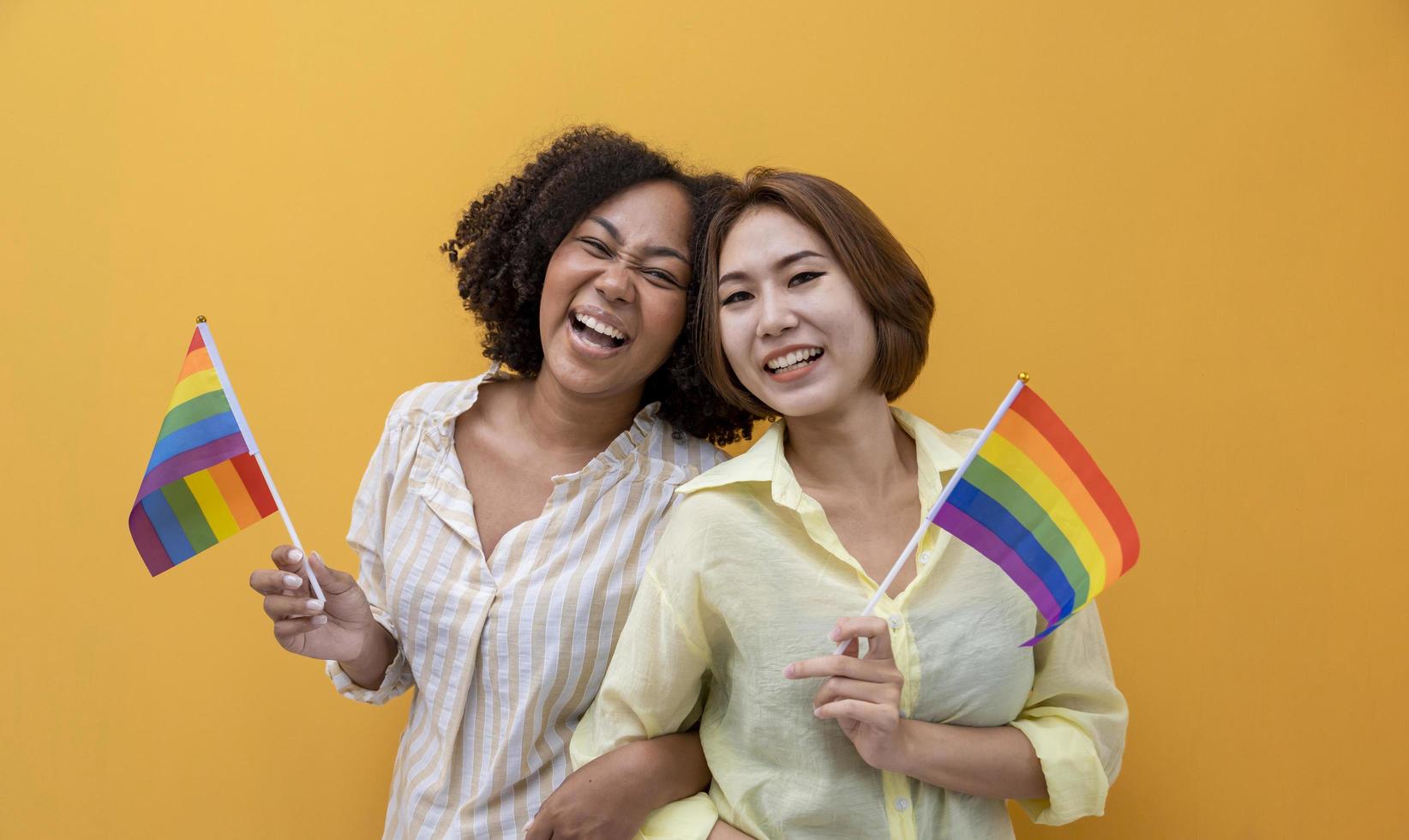 Couple of same sex marriage holding LGBTQ rainbow flag for pride month to promote equality and differences of homosexual and discrimination concept isolated on yellow background photo