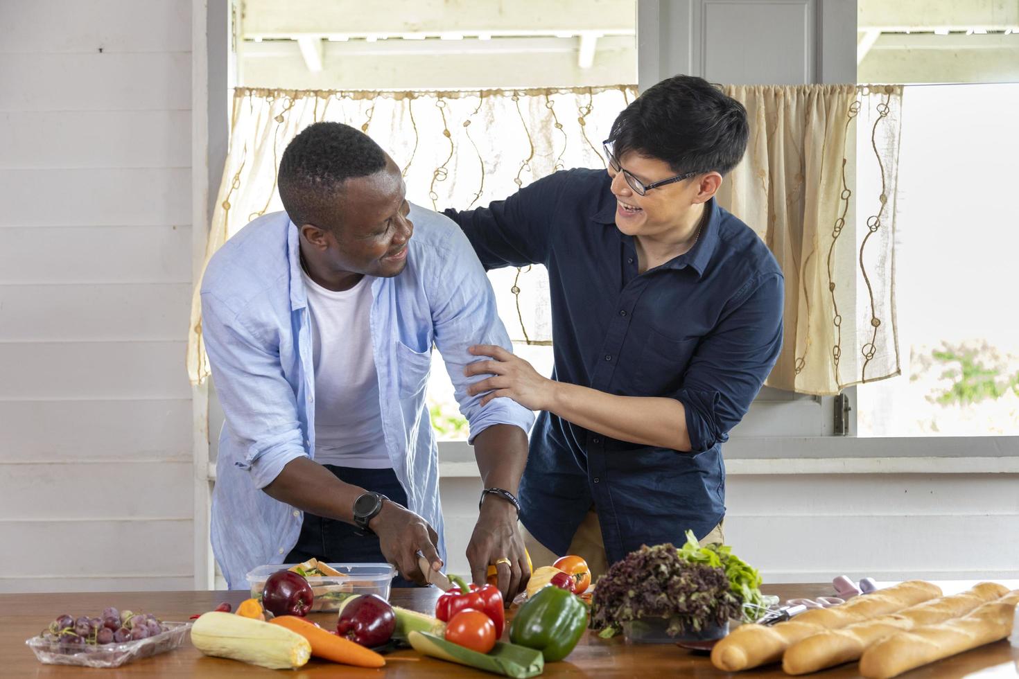 Diversity of LGBTQ gay couple between Asian and African ethnicity cooking together at home using organic vegetable to make salad and sandwich photo