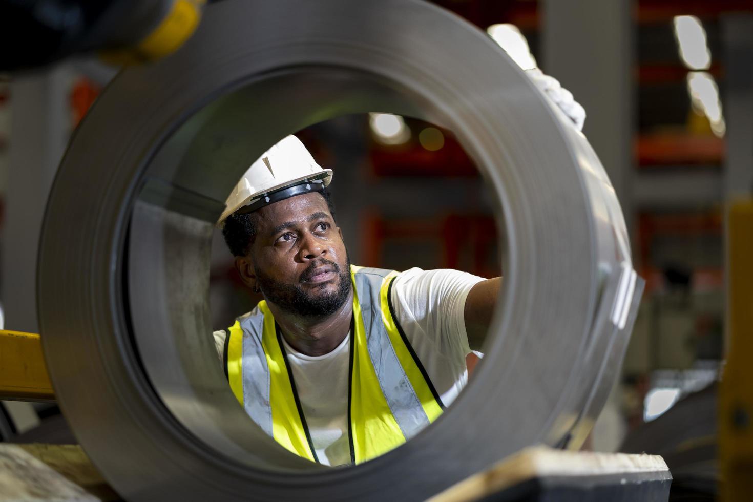 African American engineer worker is examining the stainless galvanized metal sheet roll inside the warehouse factory for roofing industry concept photo