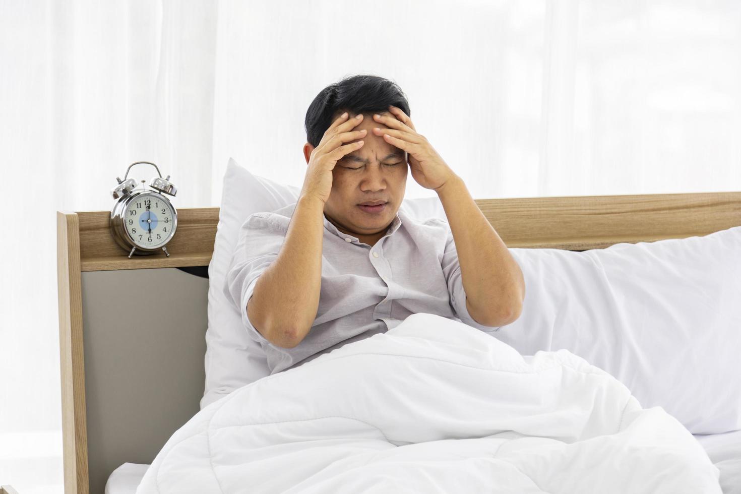 hombre infeliz sentado en su cama con estrés y preocupación que resultó en un problema de dolor de cabeza y migraña foto