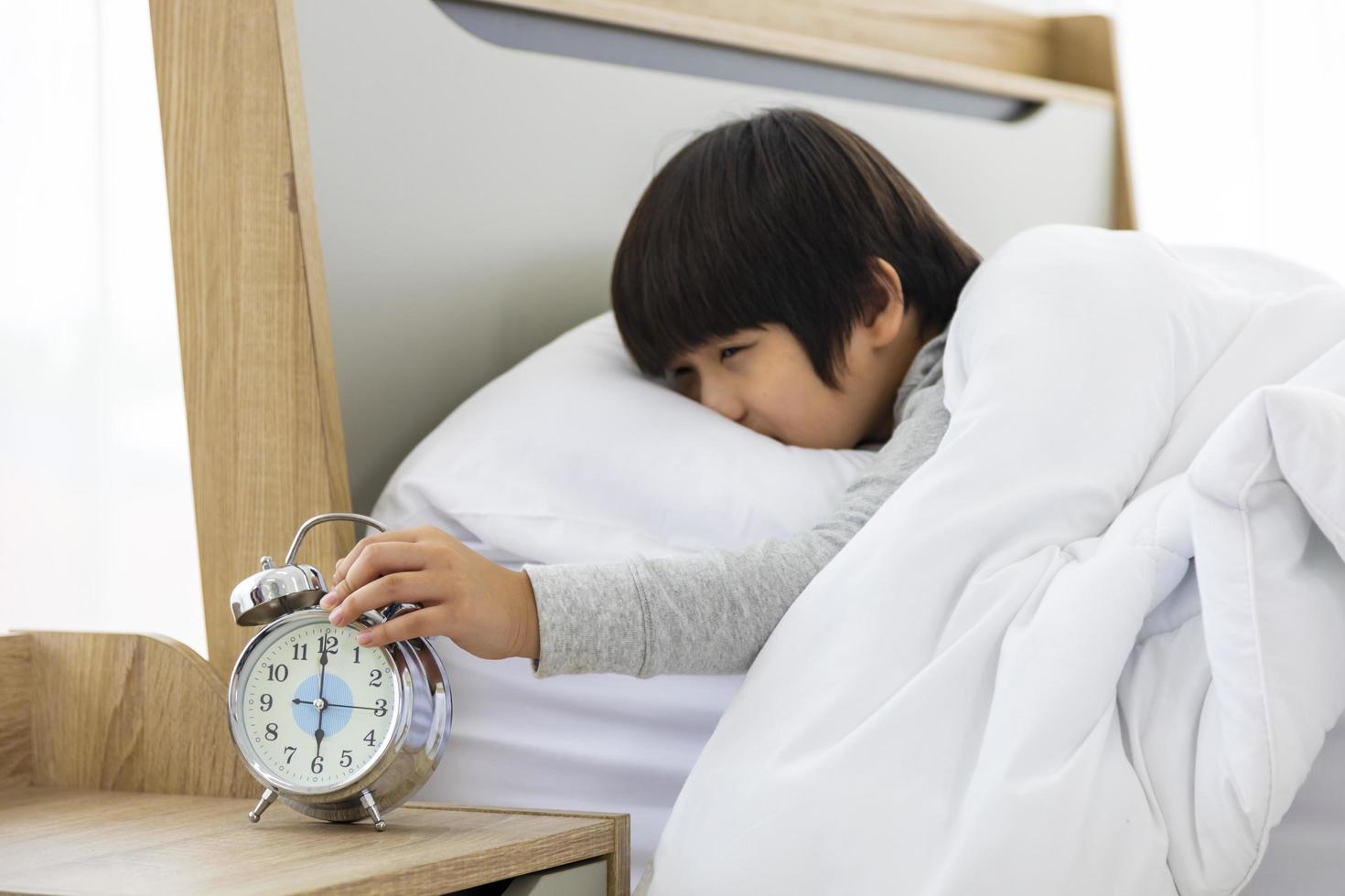 el niño apaga el despertador por la mañana y se levanta para la preparación escolar foto