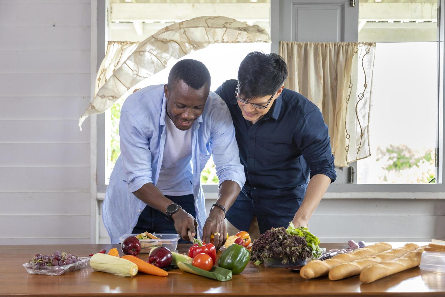 diversidad de género de la pareja gay lgbtq entre la etnia asiática y africana cocinando juntos en casa usando vegetales orgánicos para hacer ensalada y sándwich foto