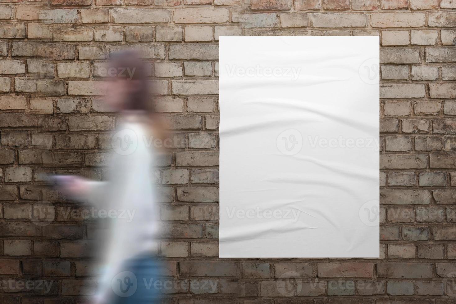 Girl walks past a white poster on brick street wall. Blank white poster with crumpled texture for design presentation photo