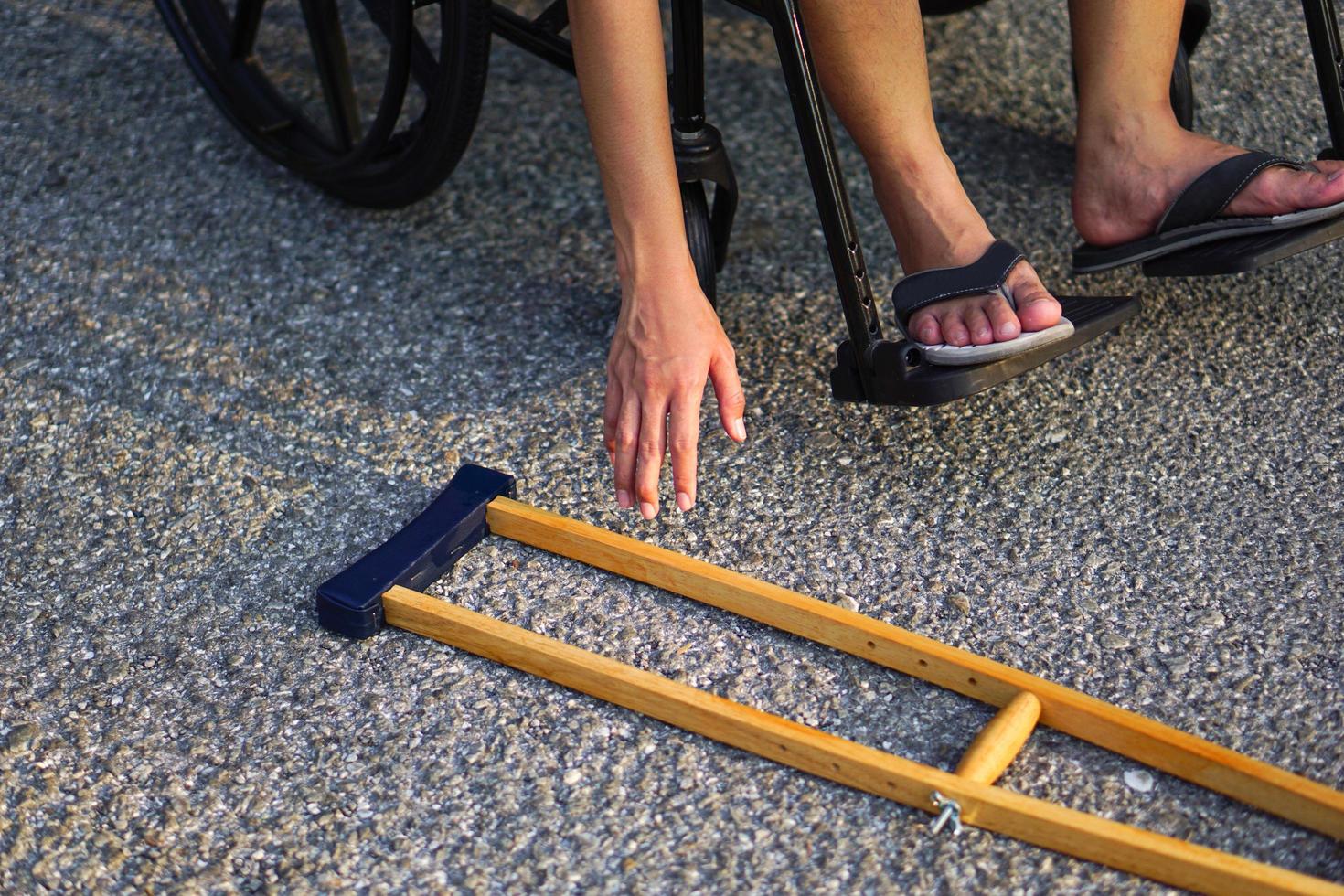 The patient sat on a wheelchair, reached his hand or bowed down, picked up a crutch on the floor. Healthcare and medical concept. photo