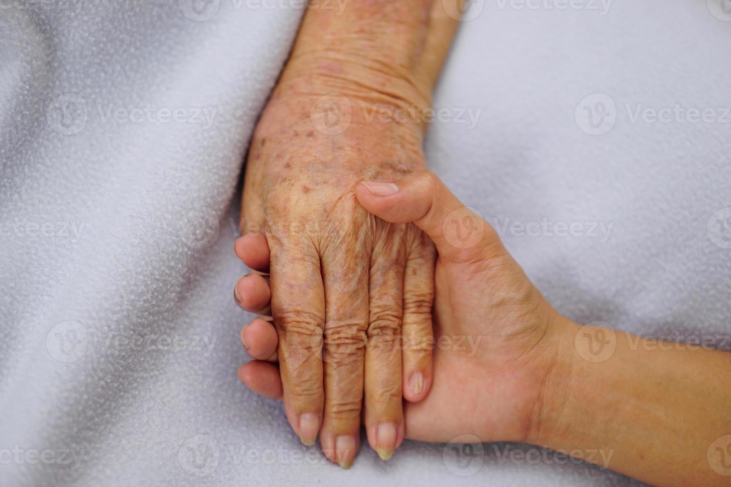 Touching or holding hands senior or elderly old woman on a blue cloth with love, care encourage and empathy. photo