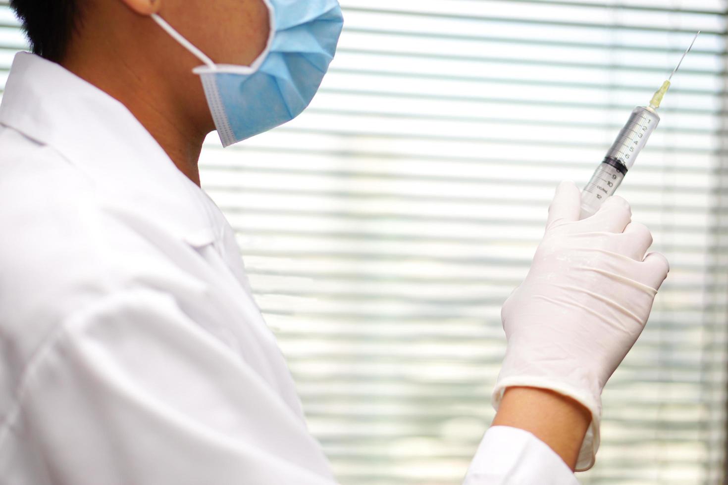 Doctor wear white coat wearing gloves and wearing a mask, holding syringe antibiotic. Healthcare and medical concept. photo