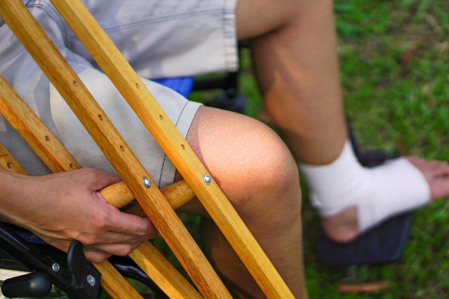 The focus image of the patient's hand holding a crutch, While sitting on a wheelchair and injured ankle. Healthcare and medical concept. photo