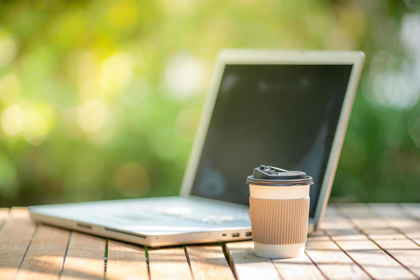 papel de taza de café con una computadora portátil en el fondo verde de la naturaleza. trabajar a distancia o desde casa. enfoque suave efecto de enfoque superficial. foto