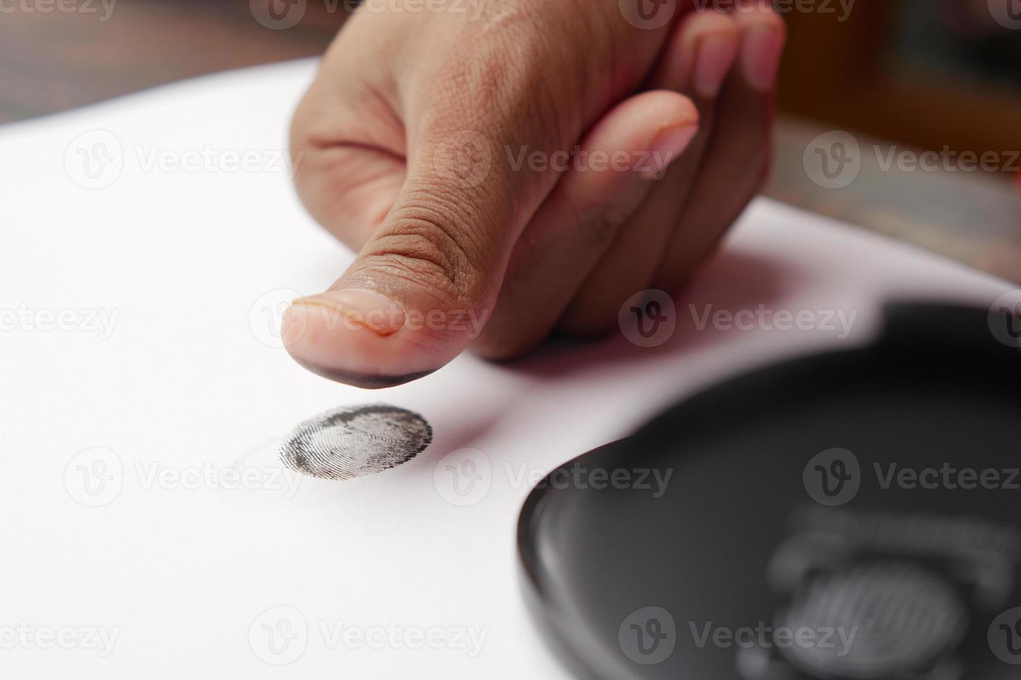 mano de persona poniendo huellas dactilares negras en un papel de cerca, foto