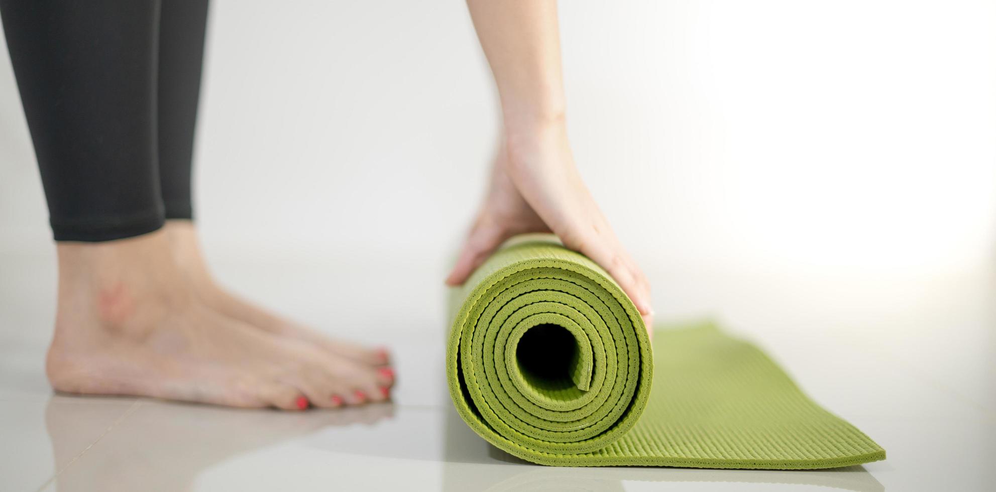 Female hand rolling green yoga mat for prepare exercise on the mat. photo