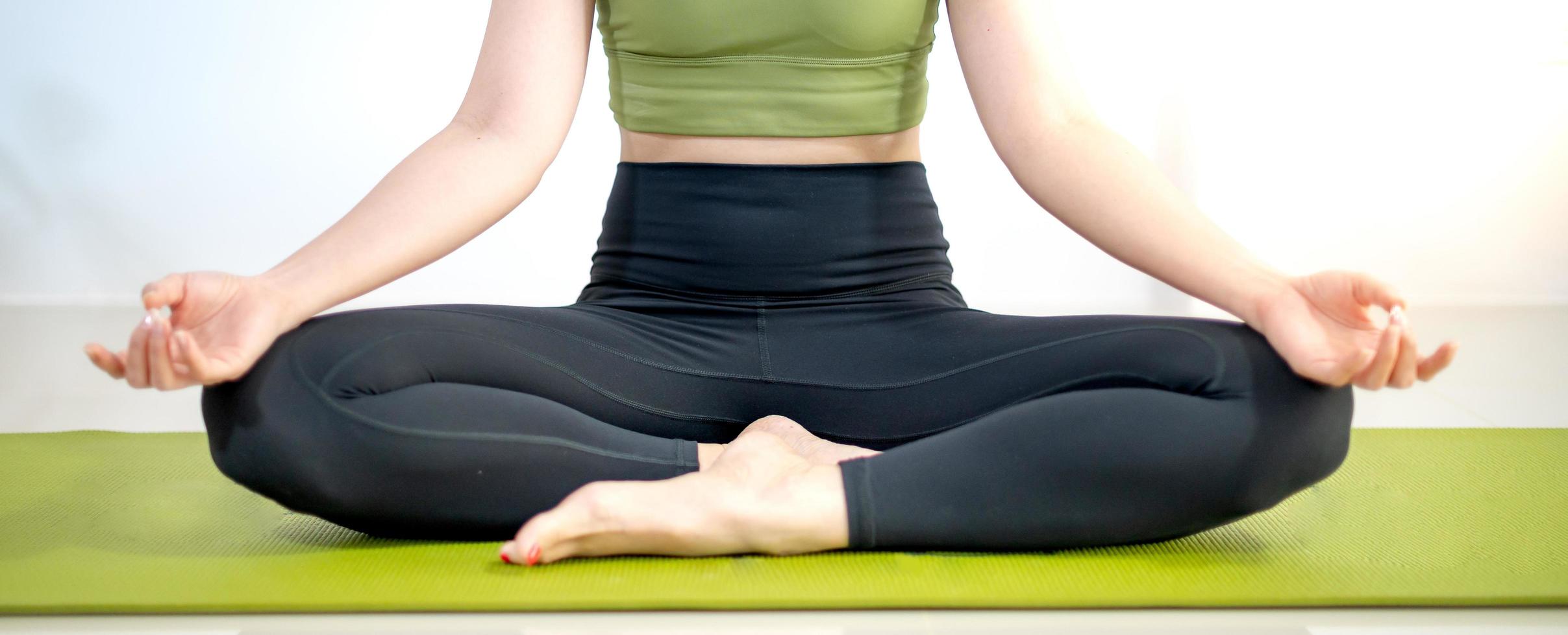 mujer practicando clases de yoga, respirando, meditando sentada en una alfombra de yoga verde, en el hogar. foto