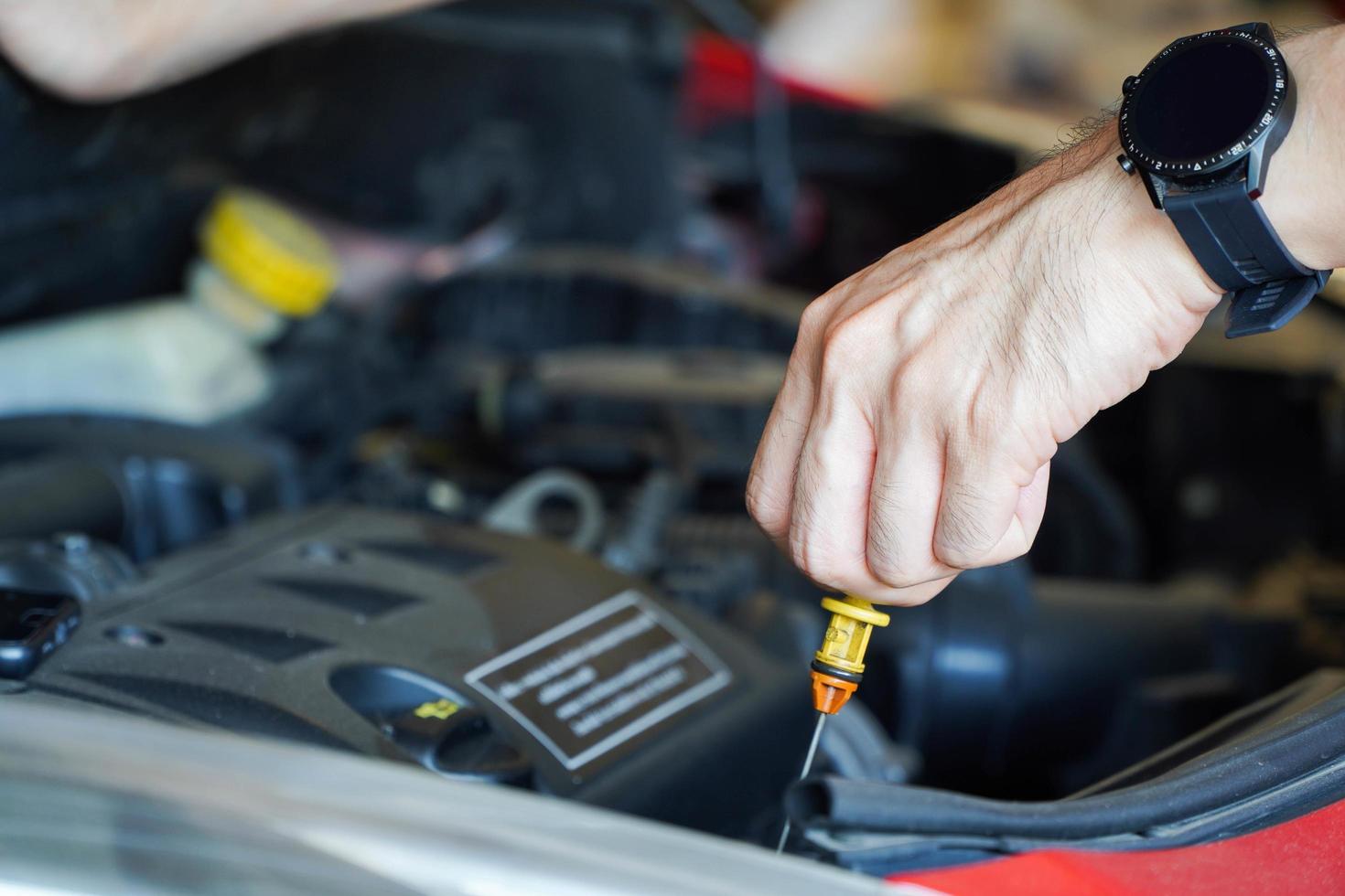 Asian mechanic repairing car with open hood,Side view of mechanic checking level motor oil in a car with open hood photo