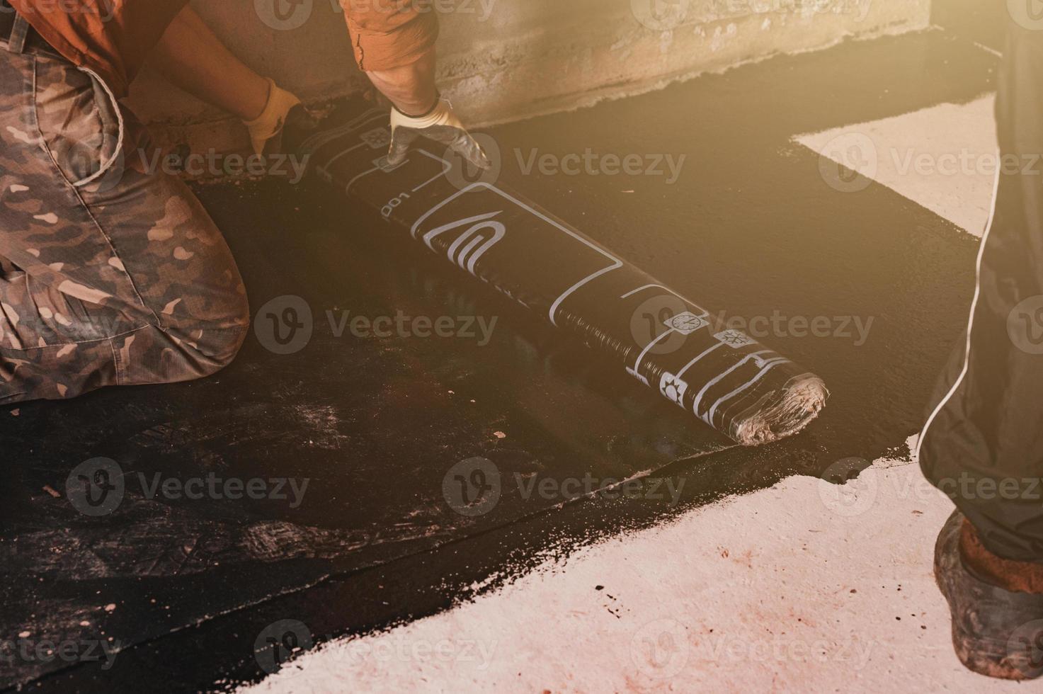 The worker untwists the roll of waterproofing and fastens it to the resin. photo