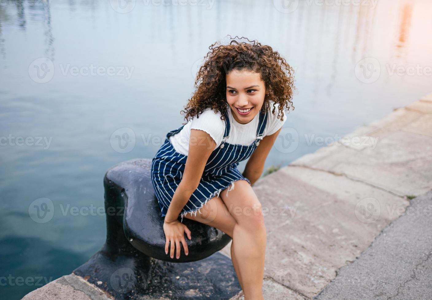 chica latina feliz sentada en un muelle foto