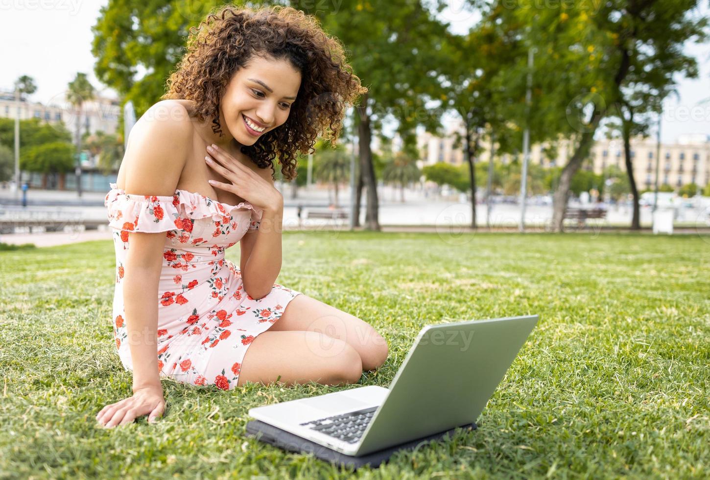 happy latina girl working with a laptop on green grass. photo