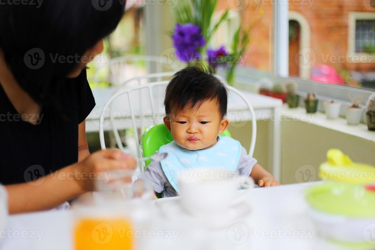 Mother feeding food to her son during breakfast at restaurant. Asian baby eating with mother. photo