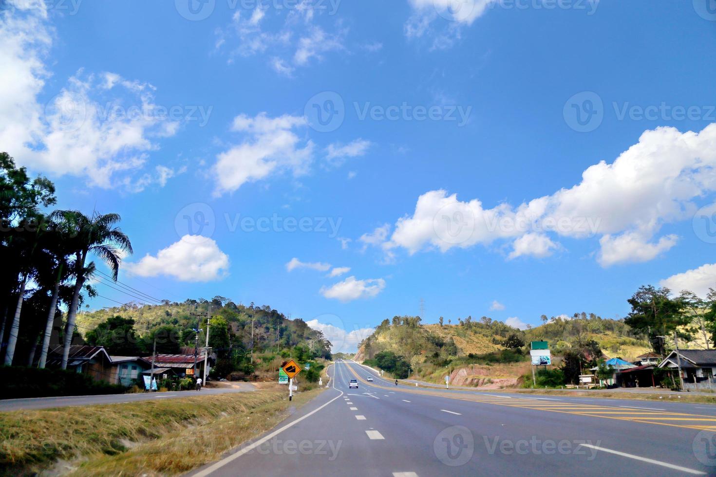 la vista de la carretera a la montaña a través de un pequeño pueblo tiene nubes y un fondo de cielo despejado. foto