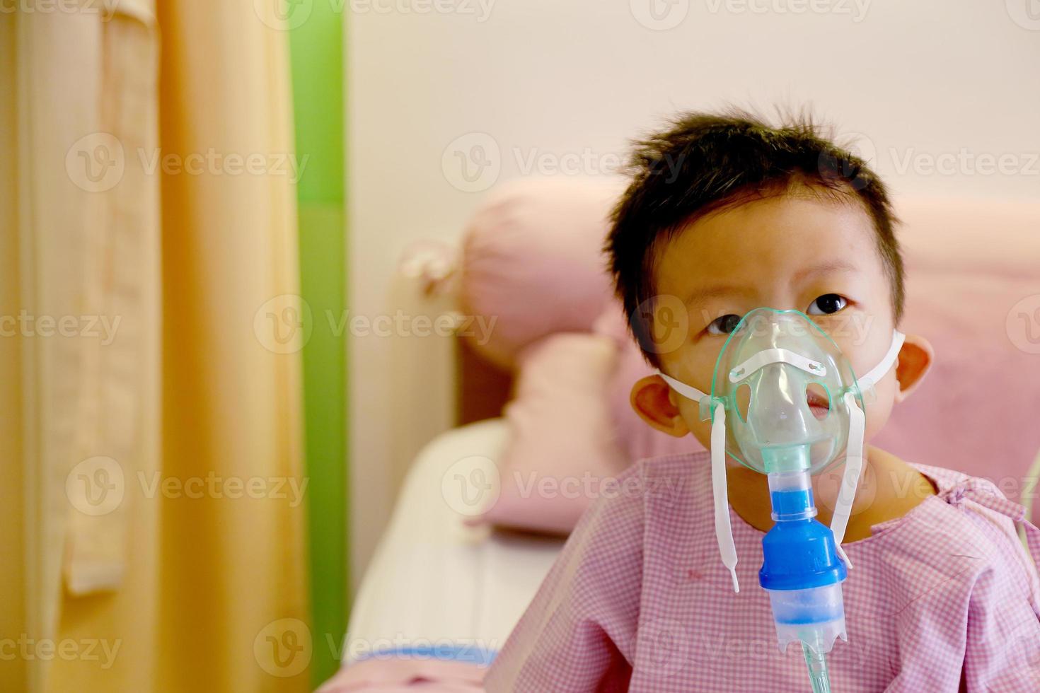 niño asiático haciendo inhalación con un nebulizador en el hospital. niño enfermo. foto