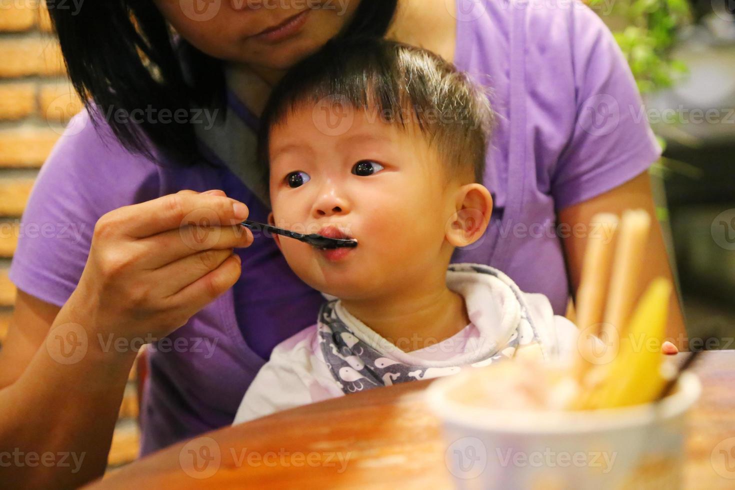 Mother feeding food to her son during dinner at restaurant. Asian baby eating with mother. photo