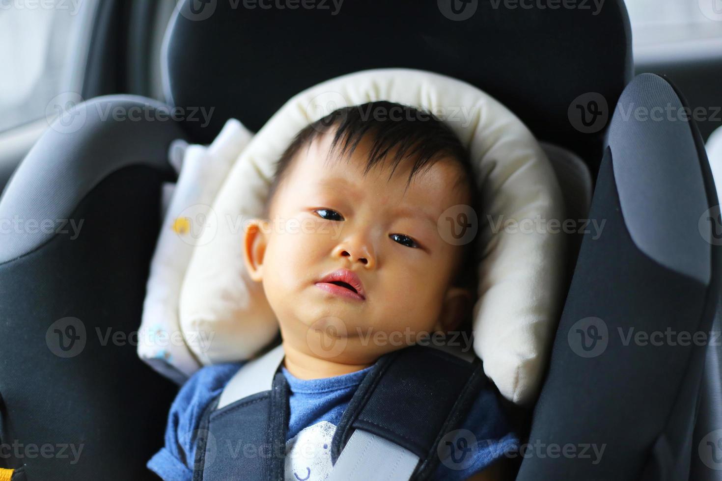 niño pequeño llorando mientras está atado en el asiento del coche de seguridad. niño asiático viajando en coche. foto