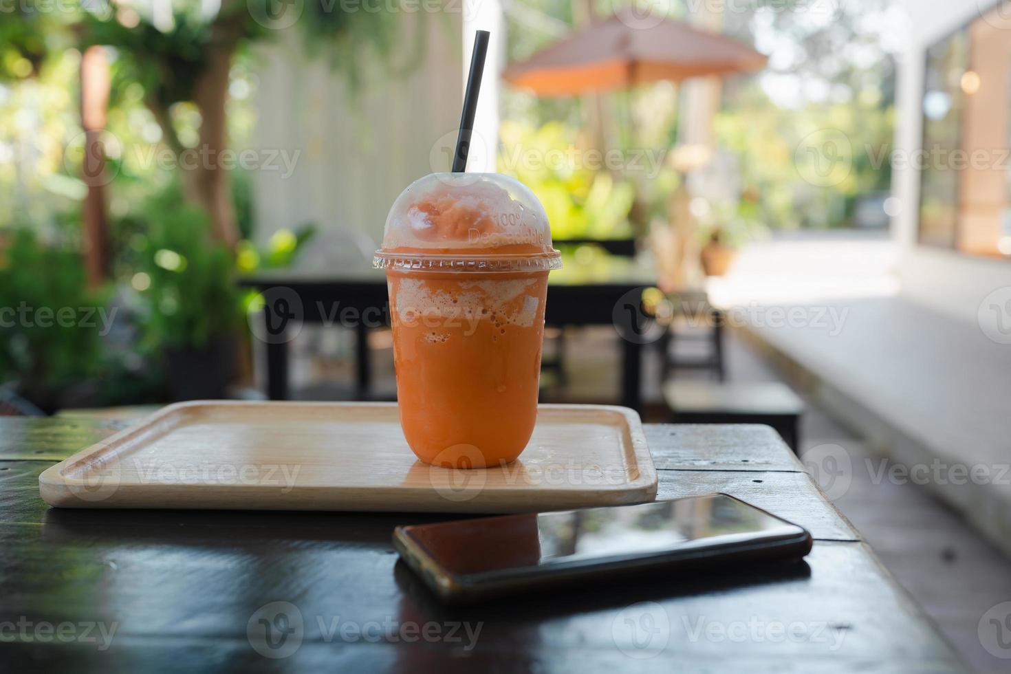 Thai milk tea frappe in takeaway cup served with wooden tray  near mobile phone photo