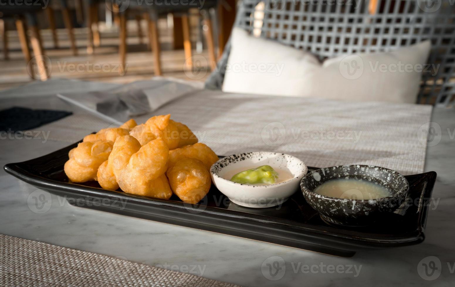 Patonggo or deep-fried dough sticks on black dish with pandan and sweet condense milk dipping on table photo