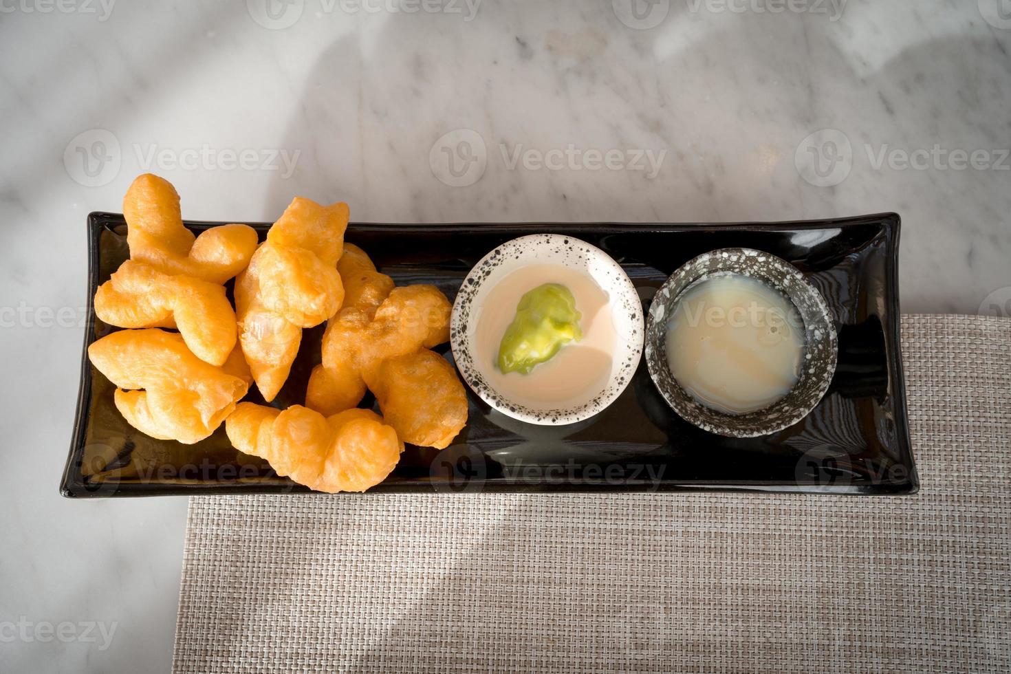 top view of Patonggo or deep-fried dough sticks on black dish with pandan and sweet condense milk dipping on table photo