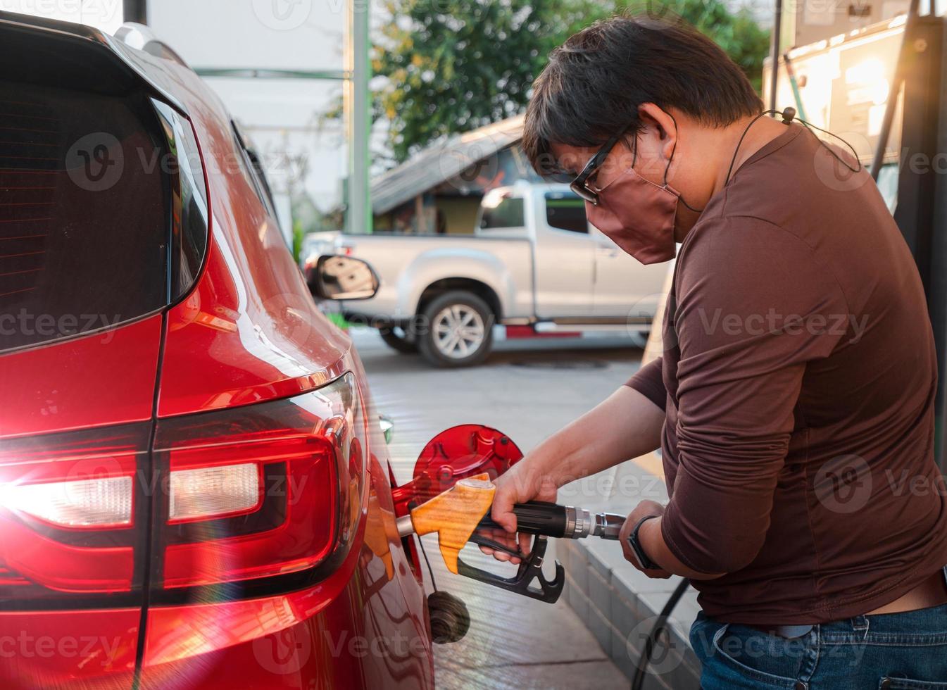 closeup man wearing fabric protective face mask hold handle gas pump tool refueling gasoline into red car photo