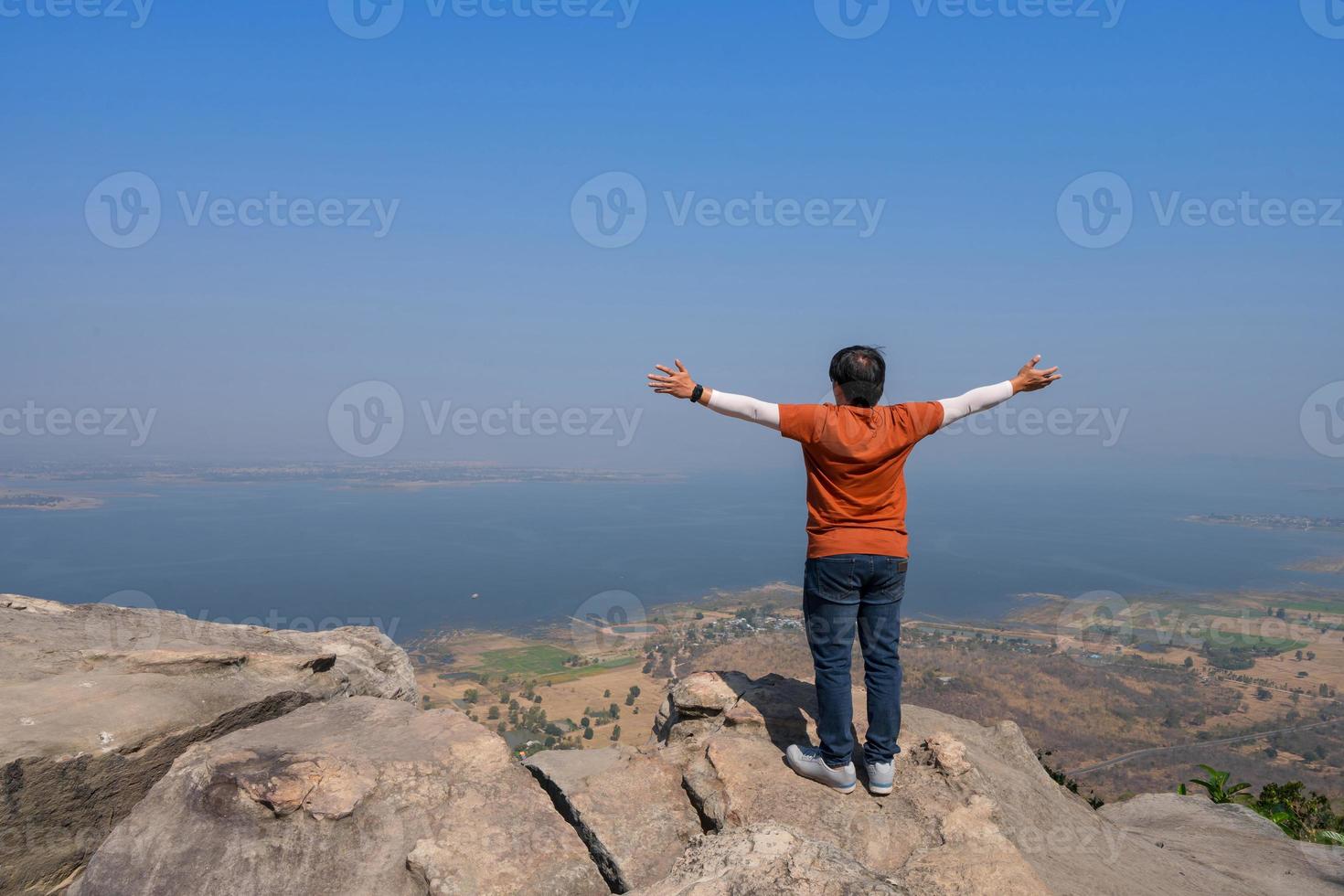 hombre en la parte de atrás con los brazos abiertos de pie sobre la roca del pico de la montaña con vistas a la presa del lago brumoso foto