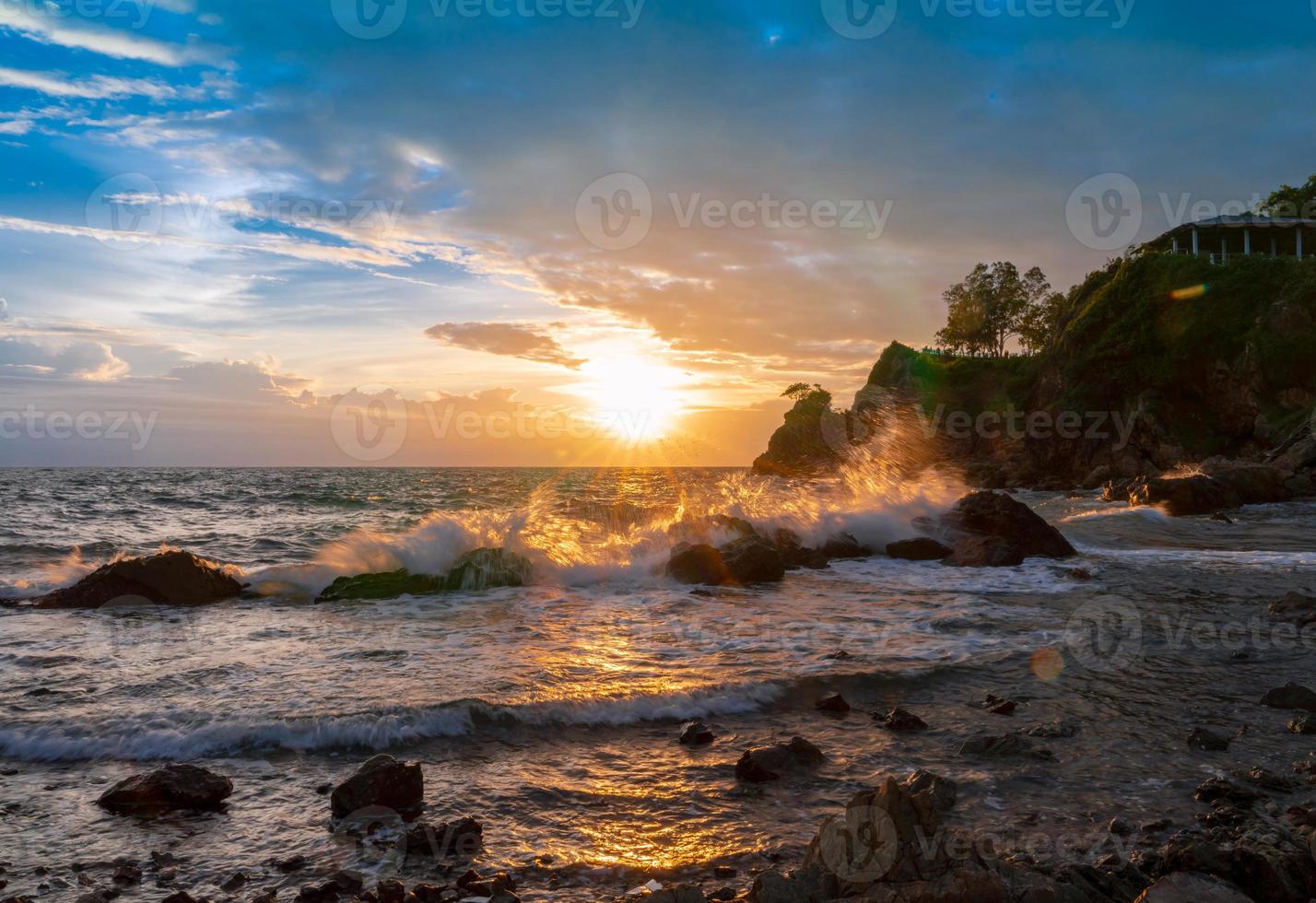 splash sea waves on rock beach with sunset rain clouds sky with light flare photo
