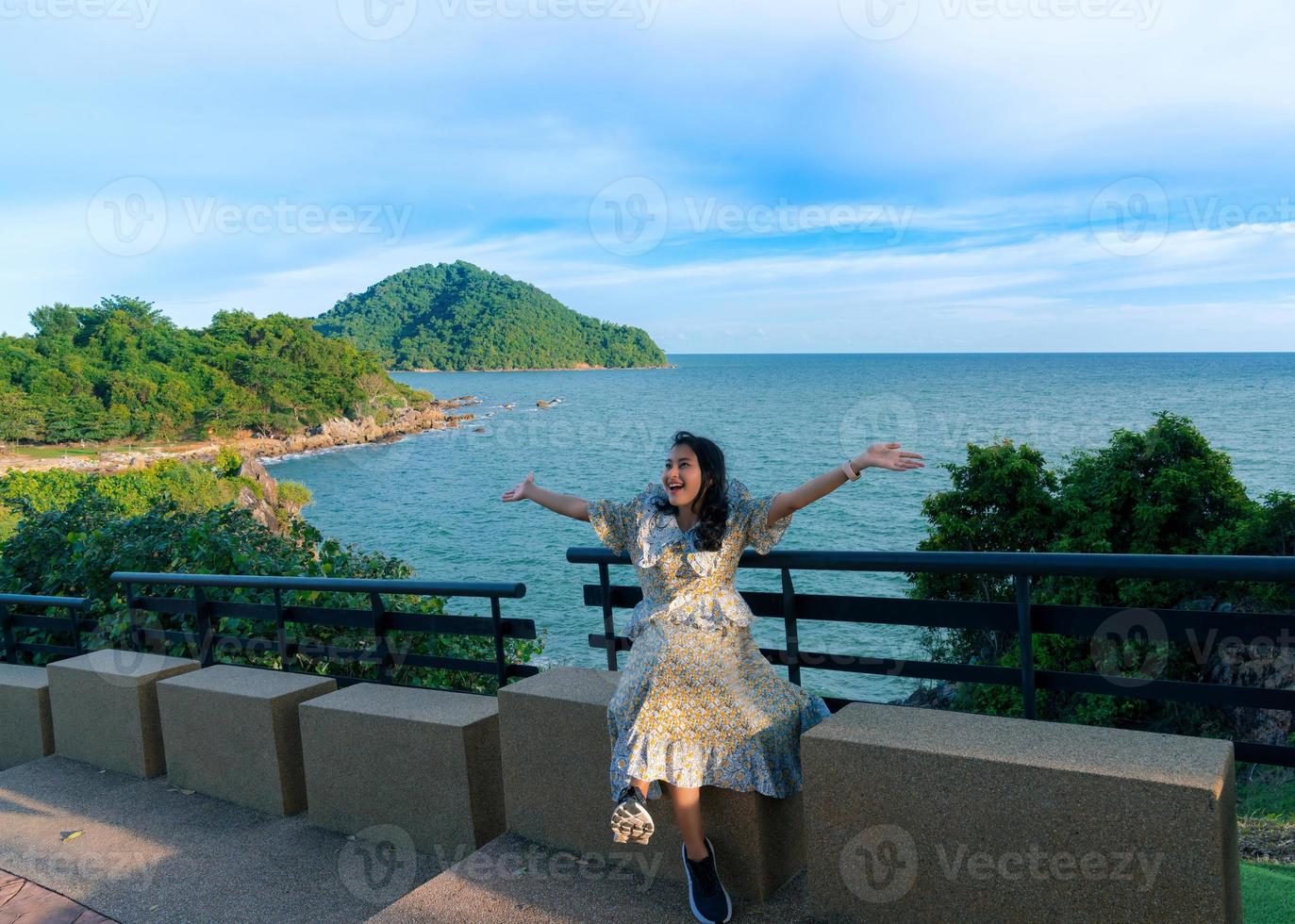 Asian woman tourist sit and feel fresh with happy arm raised at seat beside walkway on Noen Nang Phaya viewpoint with blue sea and mountain view photo