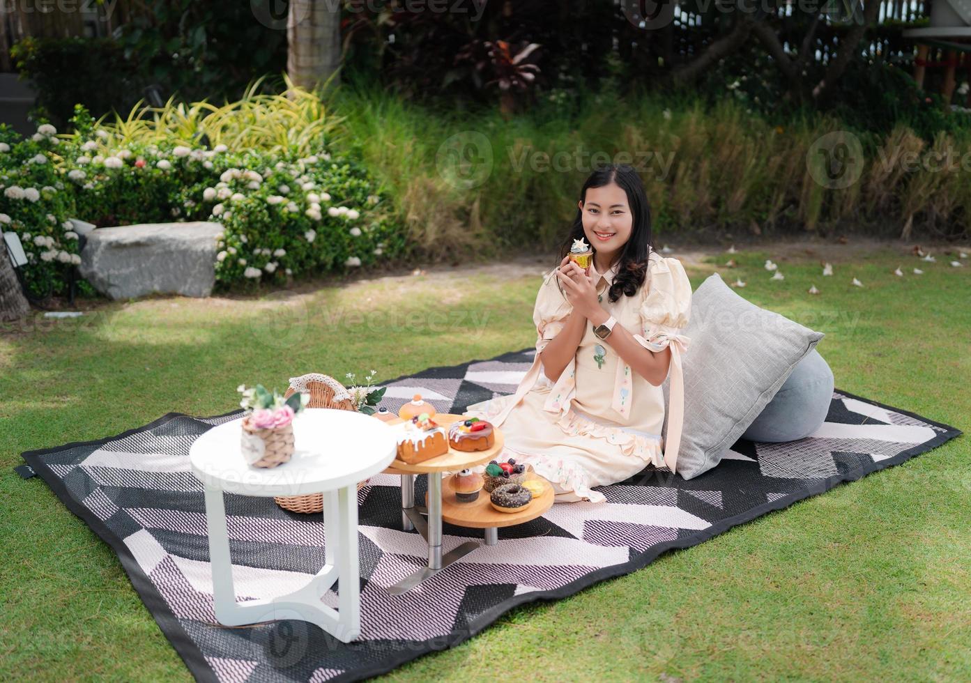 happy Asian woman enjoy picnic in fresh green garden, picnic net with snack and pillow photo
