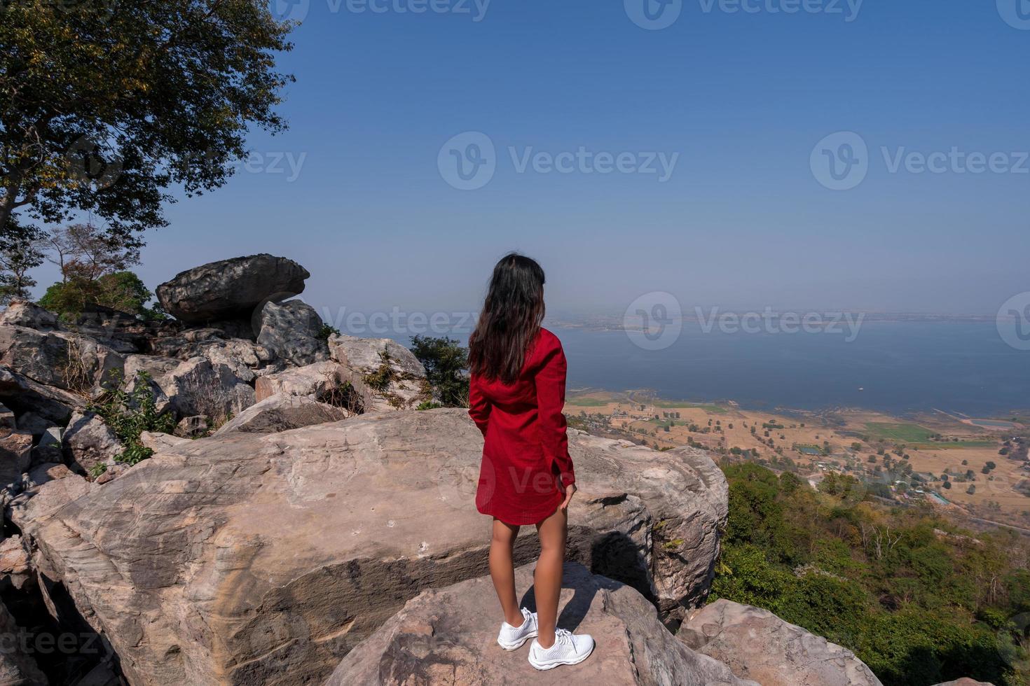 Asian woman in the back standing looking at view on rock viewpoint of mountain peak with misty lake dam view photo