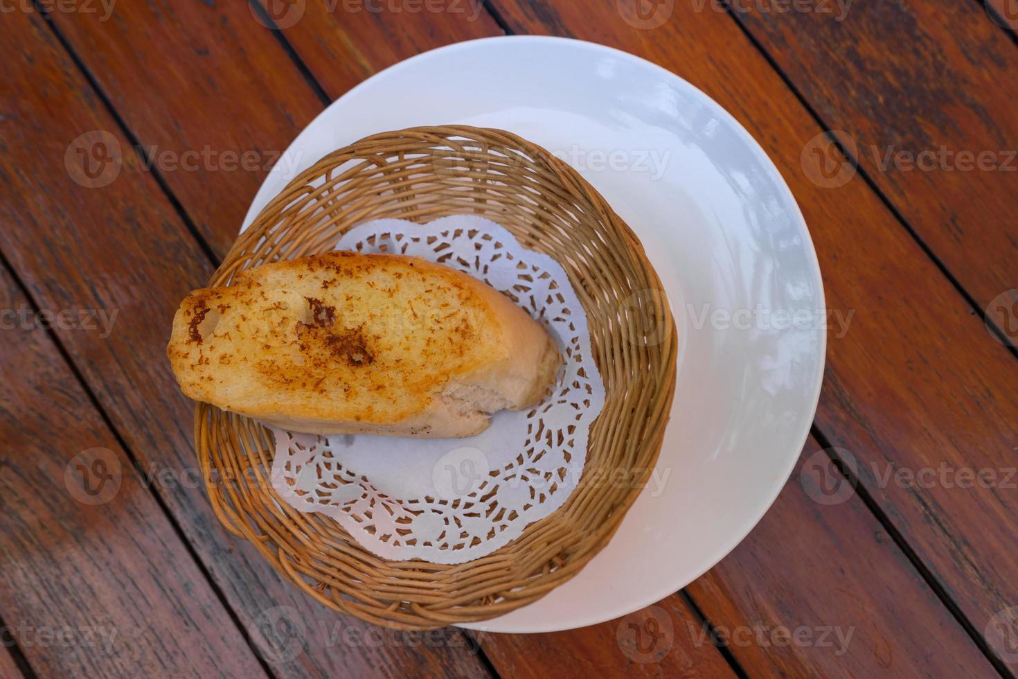 top view of garlic bread in small weaving basket on wooden table photo
