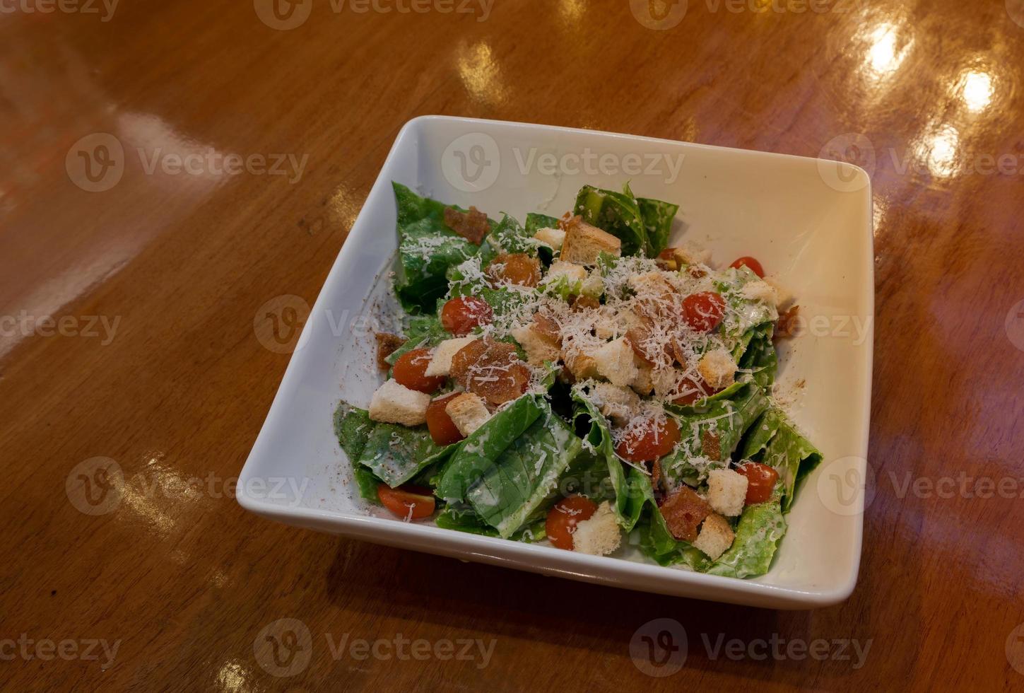 Caesar salad green salad of romaine lettuce and croutons dressed with lemon juice, olive oil, Parmesan cheese on wooden dinner table photo