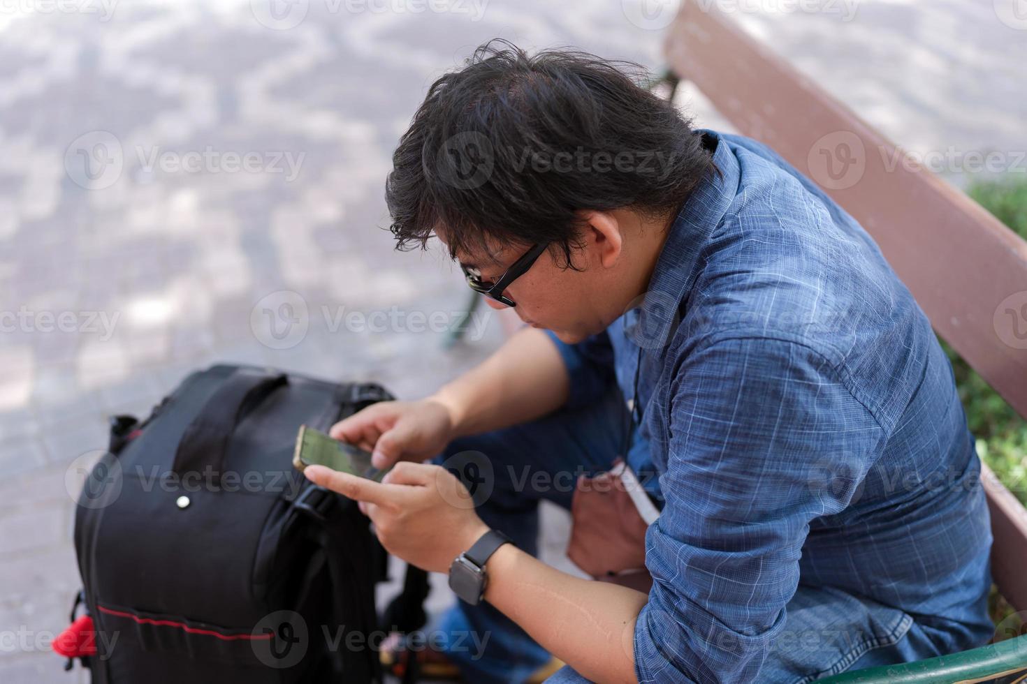 Asian tourist man with eyeglasses with luggage sit and searching for gps map photo